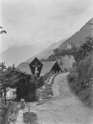 Wegekreuz im Dorf : Italien, Südtirol. Wegkreuz in Dorf Tirol bei Meran mit Blick auf Schloss Tirol