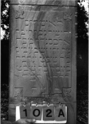Grabstein 102 (Index: 100086592) Material: Sandstein Zustand: abgeblättert Maße HxBxT: 138x57x17 cm Beschreibung: Stele, Sockel, giebelartiger Abschluß mit Verdachung Symbolik: vier Blüten: Grabstein 102A