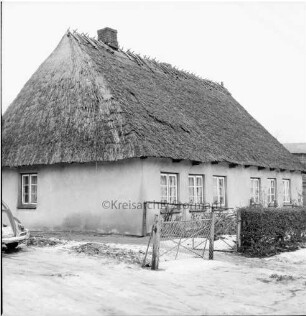 Reetdachkate: rechts Vorgarten mit Hecke und Gatter: links Pkw: Winter