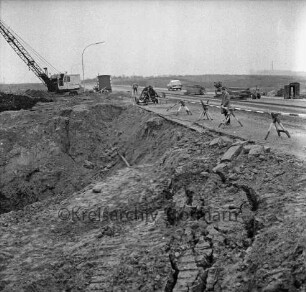 Industriestraße: Absackung eines Teilstücks: vorn Abbruchkante mit Grube: rechts Absperrung: dahinter Bagger, Arbeiter, Mann, Baubude, Baumaschinen und Pkw
