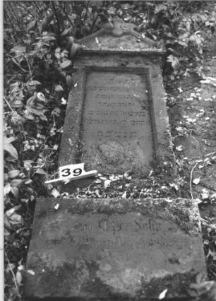 Grabstein 39 (Index: 100105999) Material: Sandstein Zustand: Stein liegend, verwittert Maße HxBxT: 174x63x16 cm Beschreibung: Stele, Sockel, giebelartiger Aufsatz mit Mittelakroter, rechteckiges Schriftfeld eingetieft: Grabstein 39