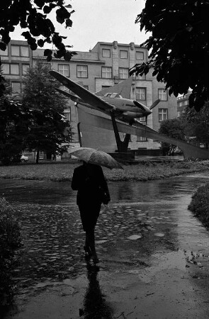 Ostrava - Ostrau : Ostrava - Ostrau (Nordmähren, Tschechoslowakei, heute Tschechien). Fußgängerin mit Regenschirm in einer Grünanlage mit Luftwaffendenkmal