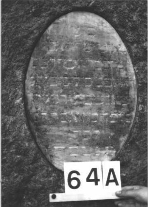 Grabstein 64 (Index: 100081668) Material: Granit, weiße Mramorplatte Zustand: verwittert, untere Schriftplatte fehlt Maße HxBxT: 146x82x40 cm Beschreibung: leicht konische Stele, gerader Abschl. , ovale Schriftplatte, querrechteckig. Schrift: Grabstein 64A