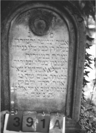 Grabstein 391 (Index: 99799648) Material: Sandstein Zustand: verwittert, Mittelaufsatz fehlt Maße HxBxT: 140x51x15 cm Beschreibung: Stele, Rundbogenabschluß, Mittelerhöhung, Mittelaufsatz fehlt, Schriftfeld eingetieft, Sockel Symbolik: Kranz: Grabstein 391A