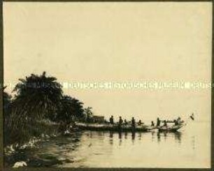 Askaris und afrikanische Helfer mit Einbaumkähnen am Ufer