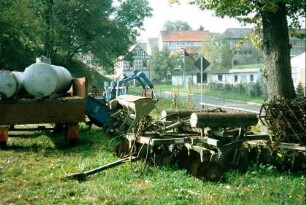 Ansammlung alter landwirtschaftlicher Geräte, dahinter Häuser