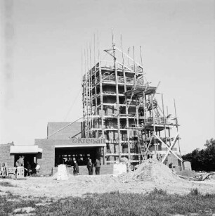 Evangelische Kirche: Rohbau: Kirchturm mit Gerüsten: Richtfest: davor Gemeindemitglieder: im Vordergrund rechts Sandhaufen und Baumaterial
