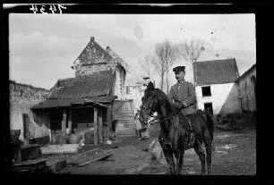 Nicht identifizierbare Ortschaft in Nordfrankreich: Offizier mit Schirmmütze zu Pferd im morastigen Hof eines landwirtschaftlichen Anwesens