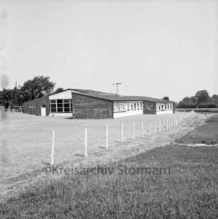Volksschule: Neubau vor Einweihung: davor neu angelegter Schulhof: vorn Zaun und Wiese
