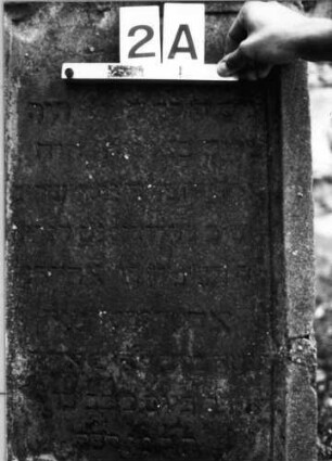 Grabstein 2 (Index: 99804491) Material: Sandstein Zustand: vom Sockel gebrochen, stark verwittert Maße HxBxT: 96x59x25 cm Beschreibung: Stele, eingezogener Segmentbogenabschluß mit Verdachung, Eckakrotere: Grabstein 2A
