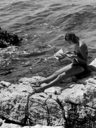 Urlaub in Jugoslawien. Eine Frau liest am felsigen Strand die Tagespresse
