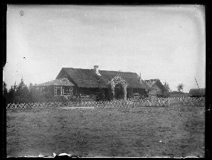 Unbekannte Ortschaft [Litauen/Weißrussland/Ukraine?]: reetgedecktes Holzhaus mit Birkenholzveranda, Birkenholzeingang, im Vordergrund ein Jägerzaun aus Birkenholz (Distanzaufnahme)
