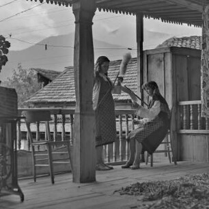 Veranda eines Wohnhauses in Bansko. Zwei junge Frauen in bulgarischer Tracht üben das Handwerk des Spinnens aus
