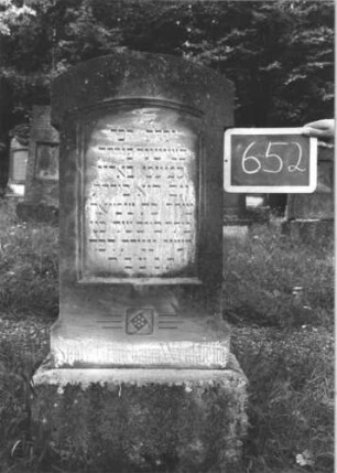 Grabstein 652 (Index: 99895245) Material: Sandstein Zustand: leicht verwittert Maße HxBxT: 124x50x21 cm Beschreibung: Stele mit überkragendem Segmentbogenabschluss; Sockel: Grabstein 652
