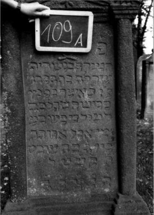 Grabstein 109 (Index: 100111225) Material: Sandstein Zustand: leicht verwittert Maße HxBxT: 150x69x21 cm Beschreibung: ädikulaartige Stele mit Halbsäulen, getreppter Sockel, giebelartiger Abschluß mit Verdachung Symbolik: gekreuzte Zweige, Blüte, Zackenfries: Grabstein 109A