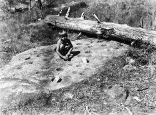 Mahlstein : Portrait eines Kindes, das auf einem mit Mörserkuhlen versehenen Felsen sitzt