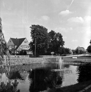 Dorfstraße: Dorfteich mit Springbrunnen: vorn links Baum: hinten Häuser und Bäume