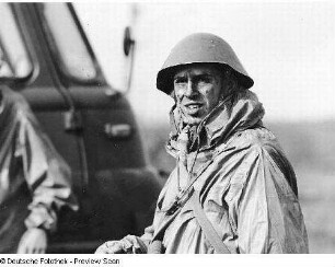Deutschland . Nationale Volksarmee - Landstreitkräfte. Soldat mit Schutzumhang (?) und Stahlhelm vor einem Kraftfahrzeug