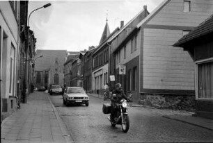 Gadebusch (Mecklenburg-Vorpommern) [Partnerstadt von Trittau]: Steinstraße: Auto, Motorräder: rechts Einmündung von Schulstraße, Personen vor Eiscafé Roller: hinten Stadtkirche St. Jakob und St. Dionysius