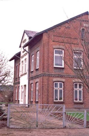 Hauptstraße 24: Bauernhaus aus Backstein, mit umlaufendem Gesims: giebelständiges Wohnhaus: rechts Straßenfront [angeschnitten]: links Traufseite mit Mittelrisalit, Eingangstür, Zwerchgiebel: vorne Einfahrt, Tor