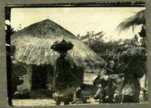 Kolonialoffizier mit afrikanischen Trägern vor einer Hütte