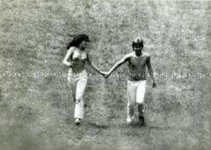 Händchen haltendes Paar läuft auf einer Sommerwiese