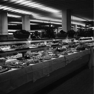 Peters Delikatessen: Mühlenstraße, Ecke Hindenburgstraße: Feinkostgeschäft: 50-jähriges Firmenjubiläum, gleichzeitig Betriebsübergabe: Innenaufnahme: Verkaufsraum: Buffet, Platten mit Speisen auf Tischtüchern: Blumenschmuck