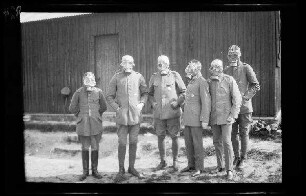 Origny (=Origny-Sainte-Benoite, Dep. Aisne, Frankreich): 6 Offiziere mit aufgesetzten Gasmasken vor einem Holzschuppen ("Gasmaskenappell")