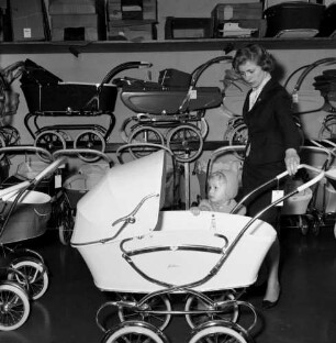 Fachgeschäft für Kinderwagen. Junge Frau mit Kind beim Betrachten eines Kinderwagens