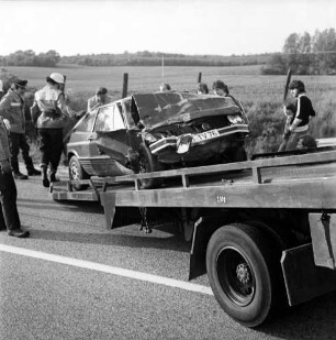 B 208: Kurve bei Westerau: Verkehrsunfall: Zusammenstoß von zwei Pkws: Feuerwehrmänner beim Aufladen von Unfallwagen mit eingedrückter Front auf Plattform von Abschleppwagen: rechts Zuschauer: Zaun, hinten Feld, im Hintergrund Wald