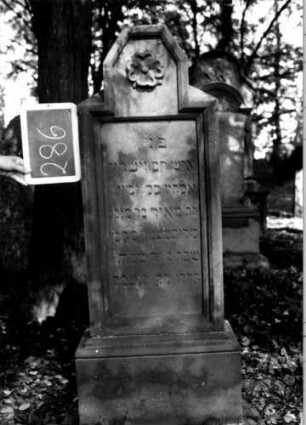 Grabstein 286 (Index: 100112044) Material: Sandstein Zustand: leicht verwittert Maße HxBxT: 137x45x20 cm Beschreibung: Stele, profilierter Sockel, Abschluß: Sonderform, rechteckiges Schriftfeld eingetieft Symbolik: Blüte: Grabstein 286