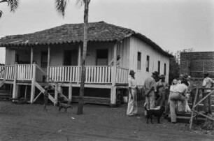 Blockhaus : Ein Blockhaus als Sitz einer Fazenda bei Votuporanga. Davor einige Männer im Kreis versammelt.
