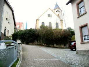 Ansicht von Westen mit Kirche (Karolingische Gründung-jetziger Baubestand 14-18 Jh) in erhöht gelegenem Kirchhof (Wehrgang der Kirchhofmauer im 18 Jh abgetragen) über dem Ort