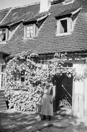 Portrait einer äteren Frau vor ihrem Haus stehend