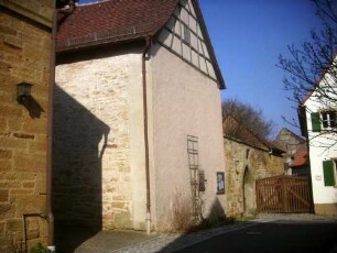 Ansicht von Südwesten mit Kirchhofmauer zur Ortsseite (originale Höhe - Schießscharten des Wehrgangs vermauert sowie einstiges Pultdach des Gaden durch Satteldach ersetzt)