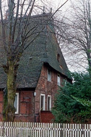 Dorfstraße 10: Schullandheim: traufständiges Fachwerkhaus mit Reetdach: Giebelseite Wohntrakt: Krüppelwalm mit Fledermausgaube, oben Verbretterung: vorne Baum, Busch, Lattenzaun