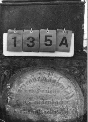 Grabstein 135 (Index: 100116062) Material: Sandstein Zustand: zum Teil verwittert mit Textverlust (besonders bei der Sockelinschrift) Maße HxBxT: 162x39x24 cm Beschreibung: doppelt aufgesockelte Stele mit Rundbogenabschluß und Aufsatz, Schriftfeld auf Stele und unterem Sockel, Sockel- Schriftfeld eingetieft mit Rundbogenabschluß: Grabstein 135A