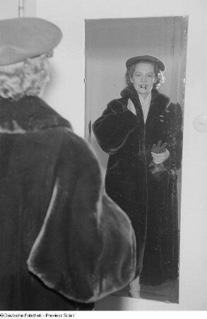 Eine Frau posiert mit Mantel und Hut vor einem Spiegel bei der "Internationalen Messemodenschau", Herbstmesse 1953