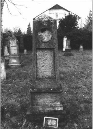 Grabstein 27 (Index: 100112301) Material: Kunststein Zustand: Schriftplatten entfernt Maße HxBxT: 200x50x47 cm Beschreibung: Obelisk, getreppter Sockel, oben runde Schriftplatte, unten rechteckige Schriftplatte: Grabstein 27