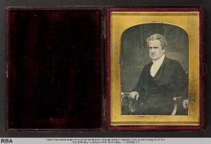Portrait eines sitzenden Mannes vor Bücherwandkulisse