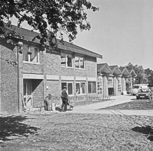 Freiwillige Feuerwehr: Stormarnstraße: Feuerwehrgerätehaus vor Fertigstellung: links zwei Arbeiter mit Schubkarre beim Verlegen von Gehwegplatten im Eingangsbereich: hinten rechts Gerüst: davor Pkw und Lieferwagen