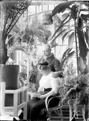 Wohnung der Familie Knochenhauer, Wintergarten? Ehepaar Fanny und Bruno Knochenhauer, ein Album oder Buch betrachtend : Kattowitz, Friedensstraße 2. Wohnung der Familie Knochenhauer, Wintergarten? Ehepaar Fanny und Bruno Knochenhauer, ein Album oder Buch betrachtend