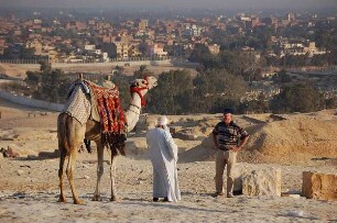 Kairo - Kamel für einen Ausritt : Kamelbesitzer verhandelt mit einem Touristen an den Pyramiden von Gizeh über einen Ausritt, Hintergrund Kairo, aufgenommen 2006