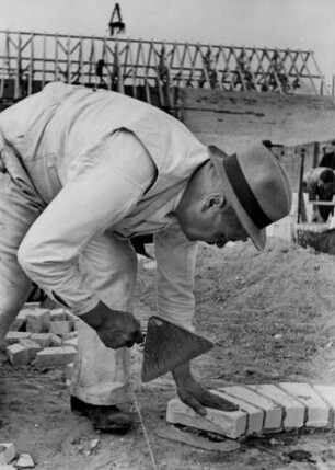 Ein Maurer bei der Arbeit. Er legt auf der Baustelle eine runde Grundmauer