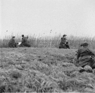 Deutsche Demokratische Republik. Grenze zwischen BRD und DDR. Offizier und Grenzpolizist bei einer Lagebesprechung mit Karte im Gelände, abseits zwei Grenzposten zur Sicherung des Abschnittes