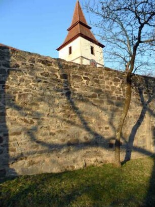 Kirchhofmauer im Süden mit Werksteinen im Mauersteinverband von der Feldseite mit Kirchturm im Glockengeschoß