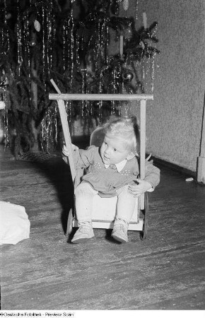 Porträt eines kleinen Mädchens mit Puppenwagen vor einem Weihnachtsbaum