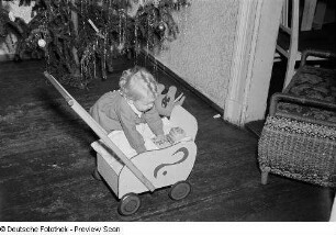 Porträt eines kleinen Mädchens mit Puppenwagen vor einem Weihnachtsbaum