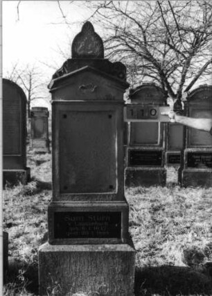 Grabstein 110 (Index: 100116426) Material: Sandstein, Granitplatte Zustand: Schriftplatte an der Stele fehlt, linker Akroter abgebrochen, ansonsten leicht verwittert Maße HxBxT: 212x54x28 cm Beschreibung: doppelt aufgesockelte Stele mit Giebelabschluß, Eckakroteren und Aufsatz, eingesetzte Schriftplatte auf Stele und oberem Sockel: Grabstein 110