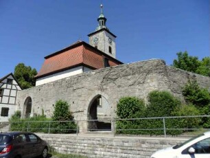 Ansicht von Südwesten mit Kirche über Kirchhofmauer (Wehrgang abgetragen) mit erhaltenem äußerenm Torbogen sowie Halbschalenturm im Südwesten)